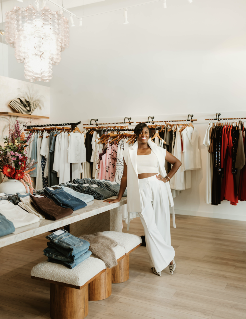 The interior of ZOË Palm Beach Gardens featuring curated clothing displays, folded apparel, and elegant boutique décor.
